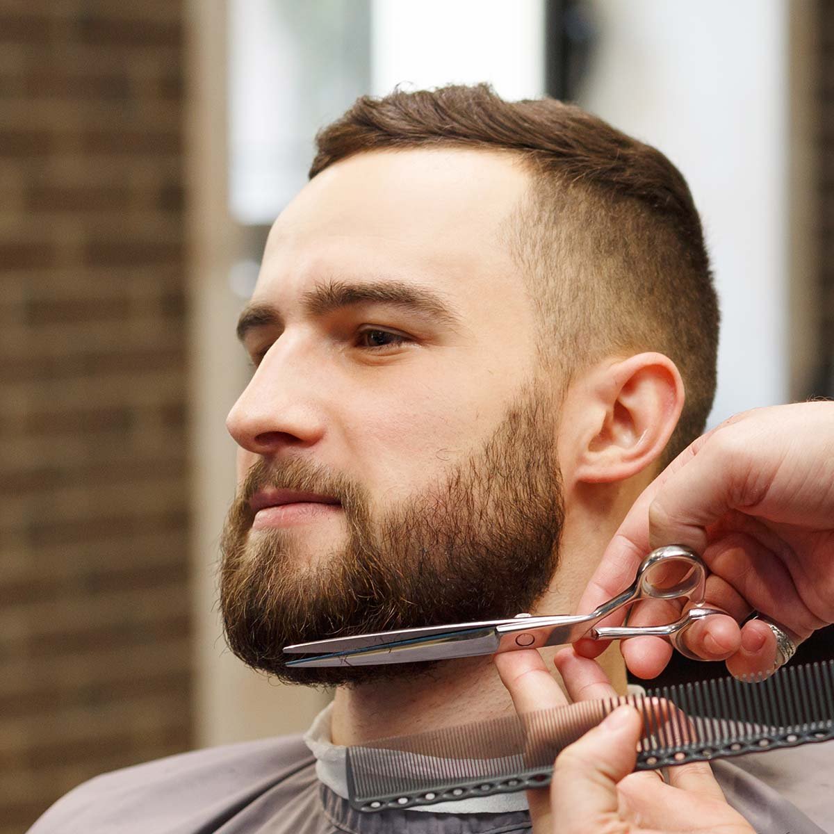 barber styling beard with scissors to client at ba M5SCQBG.jpg